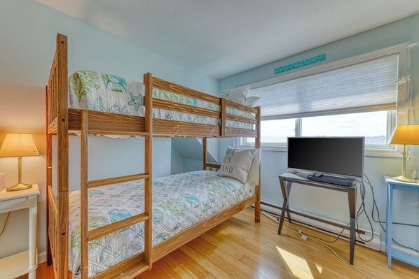 A bunk bed with a TV stand and a window with blinds.