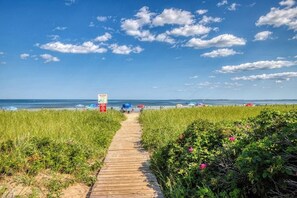 A wooden boardwalk leading to a beach with umbrellas and a sign.