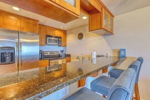 A kitchen with wooden cabinets, stainless steel appliances, a granite countertop, and a built-in bar area with seating.