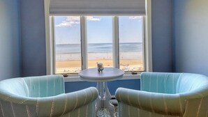 Ein Zimmer mit Blick auf den Strand, zwei gepolsterte Sessel, ein kleiner Tisch und ein Fenster mit Jalousien.