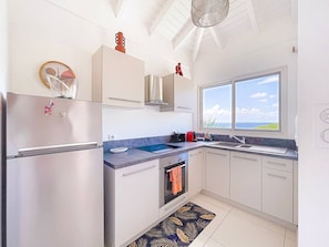 A modern kitchen with a stainless steel refrigerator, a built-in oven, a window with a view, and a ceiling fan. - Koala 2, elegant studio with sea view in Anse Marcel (Anse Marcel)