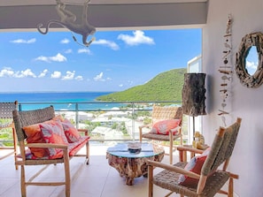 A balcony with wicker furniture, a round glass table, and a view of the ocean and hills. - Koala 2, elegant studio with sea view in Anse Marcel (Anse Marcel)