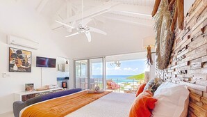 Quarto com cama, ventilador de teto, televisão e vista para o oceano.