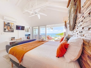 A bedroom with a bed, a ceiling fan, a TV, and a view of the ocean. - Koala 2, elegant studio with sea view in Anse Marcel (Anse Marcel)