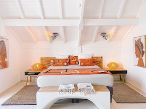 Ein Schlafzimmer mit Bett, Kopfteil, Nachttischen, Lampen und Kunstwerken.