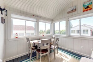 A sunroom with a table and chairs, large windows, and a view of a house.