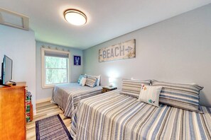 A bedroom with two beds, a window, a wall sign reading 'BEACH,' and a ceiling light.