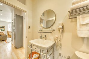 Un baño con un lavamanos blanco, un espejo redondo, un secador de pelo y un perchero para toallas.