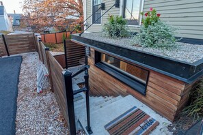 Eine moderne Außenterrasse mit Holzgeländer, einem kleinen Fenster und einem Kiesbereich mit Pflanzen.