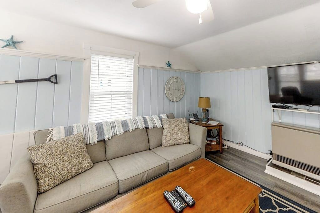A living room with a sofa, a coffee table, a TV, and a clock on the wall.