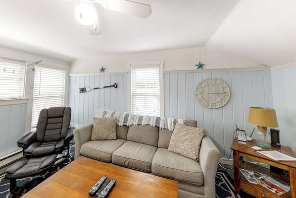 A living room with a sofa, a recliner, a coffee table, a lamp, and a wall clock.