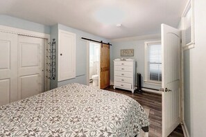 A bedroom with a bed, a dresser, a door, and a window.