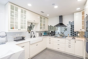 A modern kitchen with white cabinetry, a black range hood, and a hexagonal tile backsplash.