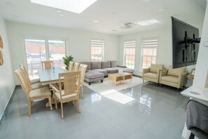 A modern living room with a dining table, sofas, and a TV mounted on the wall.