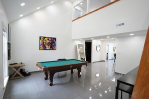 A spacious indoor area with a pool table, a painting on the wall, and a wooden bench.