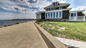 A modern two-story house with a stone facade, large windows, and a balcony overlooking a beach. - Coastal gem on the water with beach access, gorgeous views & spacious layout (Wells)