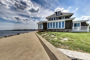 Ein modernes, zweistöckiges Haus mit Steinaußenwand, großen Fenstern und einem Balkon mit Blick auf einen Strand.
