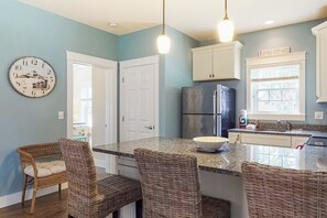 Une cuisine avec un îlot central, des chaises en osier, une horloge et un panneau sur la fenêtre.