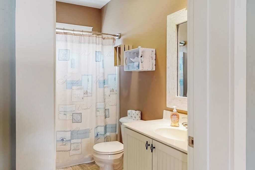 A bathroom with a toilet, a shower curtain, a sink, and a mirror.