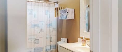 A bathroom with a toilet, a shower curtain, a sink, and a mirror.
