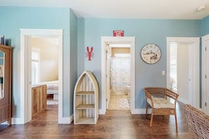 A hallway with a wooden floor, a wicker chair, and a wall clock.