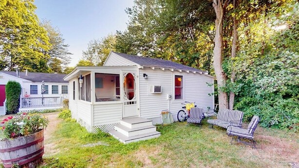 En etagers mobilhome med veranda, en lille terrasse med udendørs møbler, og en cykel parkeret udenfor.
