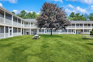 A motel with a central lawn, picnic tables, and a large tree. - Inviting condo with high-speed WiFi and shared indoor pool - two miles to beach (Wells)