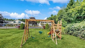 A wooden swing set in a grassy yard with houses in the background. - Inviting condo with high-speed WiFi and shared indoor pool - two miles to beach (Wells)