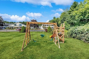 A wooden swing set in a grassy yard with houses in the background. - Inviting condo with high-speed WiFi and shared indoor pool - two miles to beach (Wells)