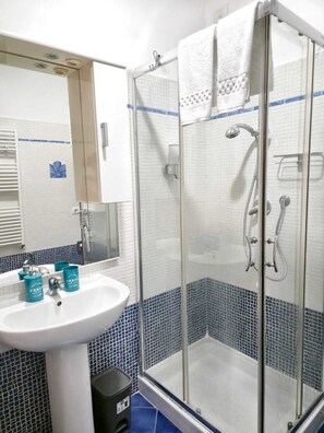 Ein Badezimmer mit einem weißen Waschbecken, blau gefliesten Wänden, einer Duschkabine aus Glas und einem Spiegel über dem Waschbecken.