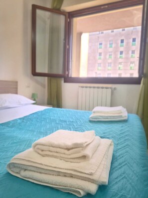 Ein Hotelzimmer mit Bett, Fenster mit Blick auf Gebäude, Heizkörper und Spiegel an der Wand.