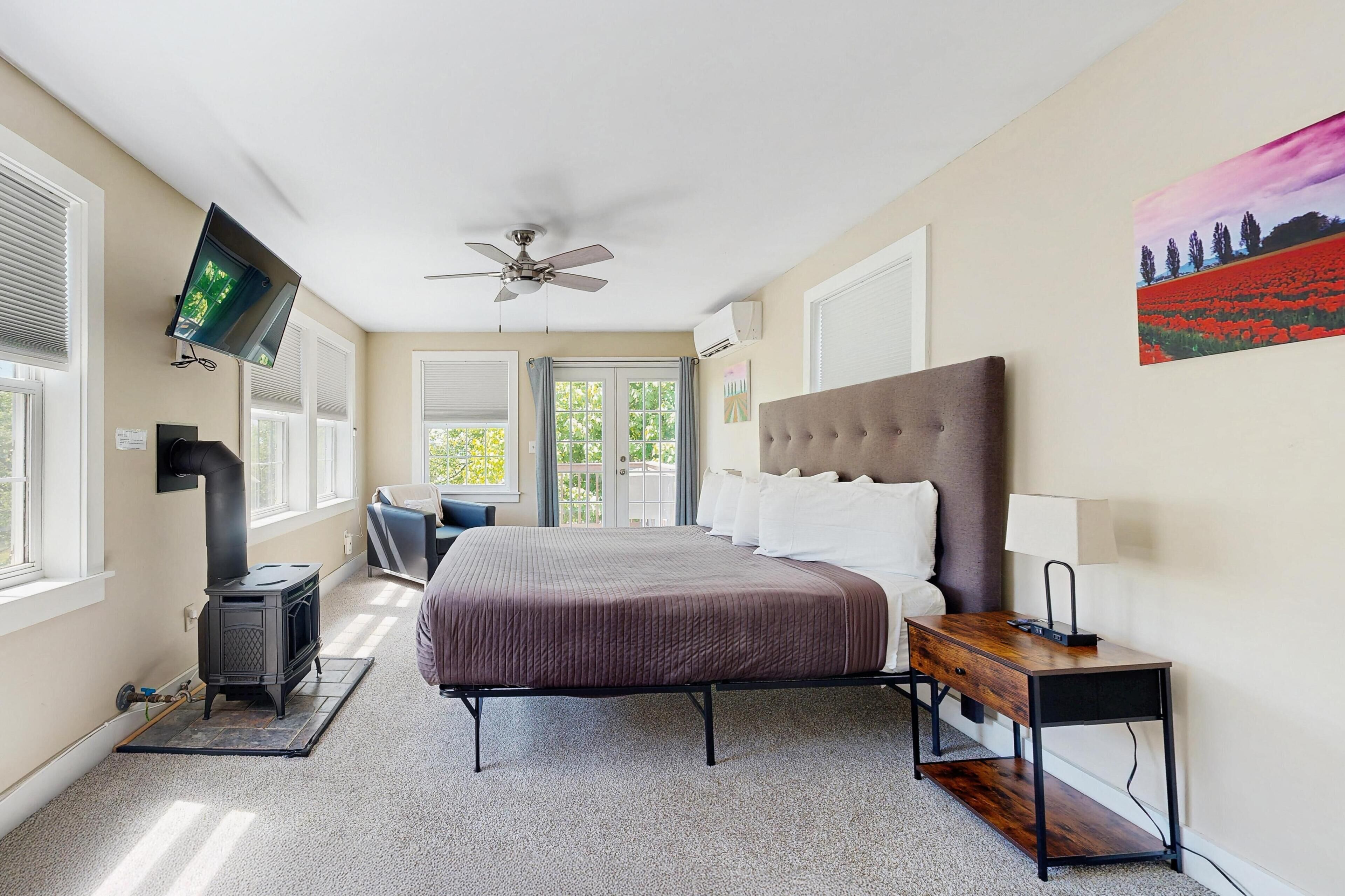 A bedroom with a bed, a heater, a TV, a ceiling fan, and a painting on the wall.