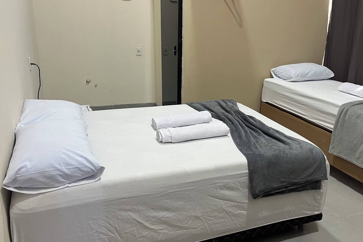 Deux lits simples avec du linge de lit blanc, une couverture grise sur le lit de gauche et une serviette grise sur le lit de droite.