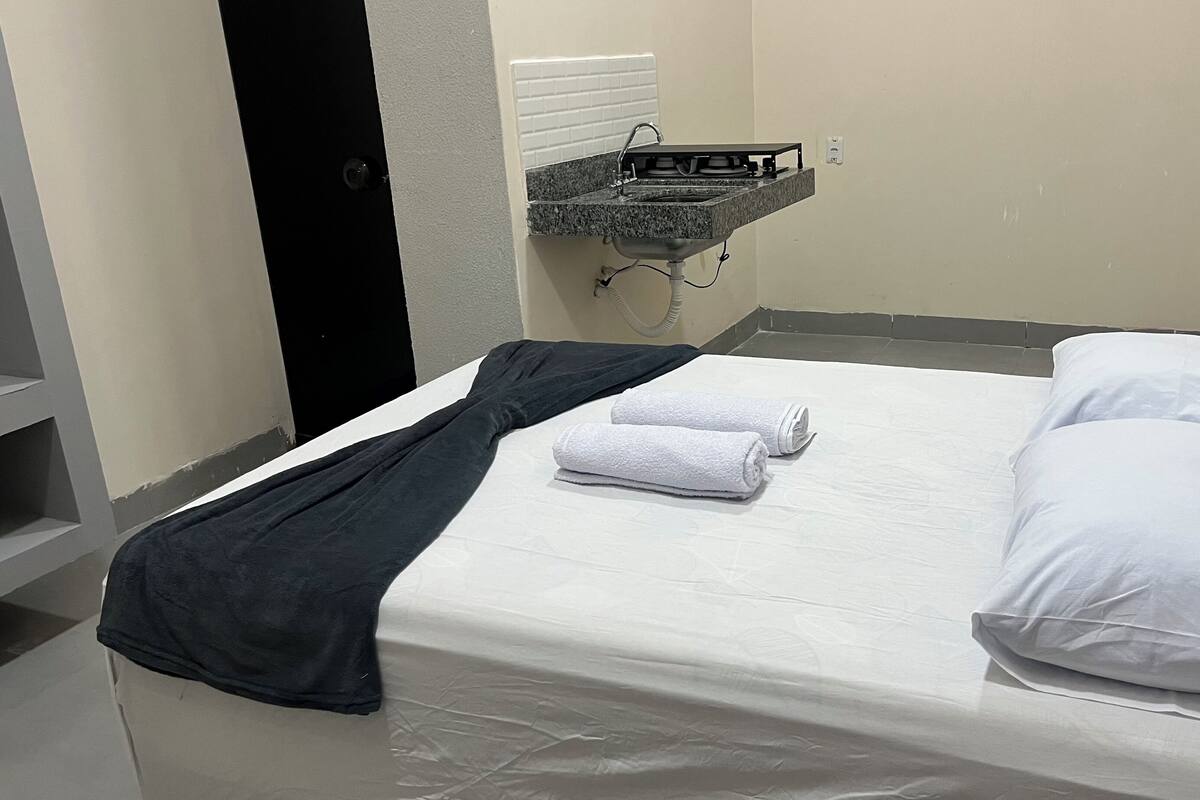 Un lit simple avec du linge de lit noir et blanc, un petit lavabo avec un miroir et un porte-serviettes.