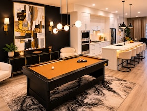 A modern living room with a pool table, a bar area, and a kitchen. - Diamond Lux | Brand New 3BR + Bonus Room | Sleeps 8+ | 10mins from Stampede park (Calgary)