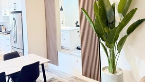 Moderni keittiö, jossa on valkoiset kaapit, ruostumattomasta teräksestä valmistettu jääkaappi sekä ruokailutila, jossa on pöytä ja tuolit.