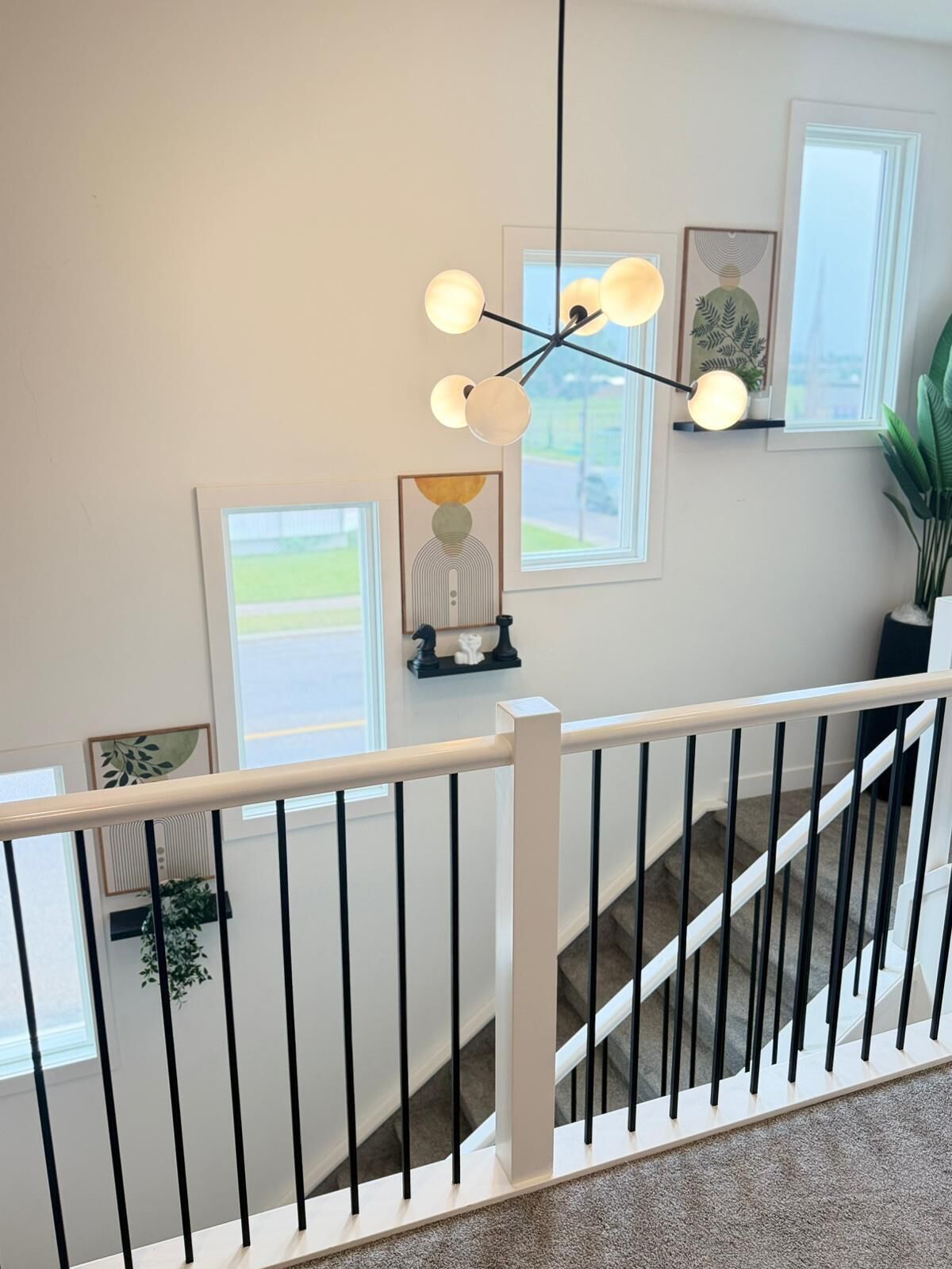 Un escalier avec une rampe blanche, un luminaire suspendu et des œuvres d’art encadrées accrochées aux murs.