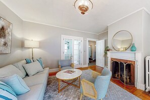 Ein Wohnzimmer mit einer Couch, Sesseln, einem Couchtisch, einem Kamin und einer Tür zu einem anderen Raum.
