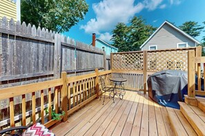 A wooden deck with a table and chairs, a barbecue grill, and a wooden fence.