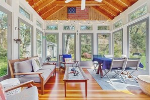 Ein geräumiges Zimmer mit Holzbalkendecke, großen Fenstern, einer Couch, einem Esstisch und einer Flagge.