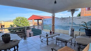 A covered outdoor area with tiled flooring, a table with a vase and a potted plant, and a seating area with cushions. - Special house to spend a pleasant time (El Caballito)