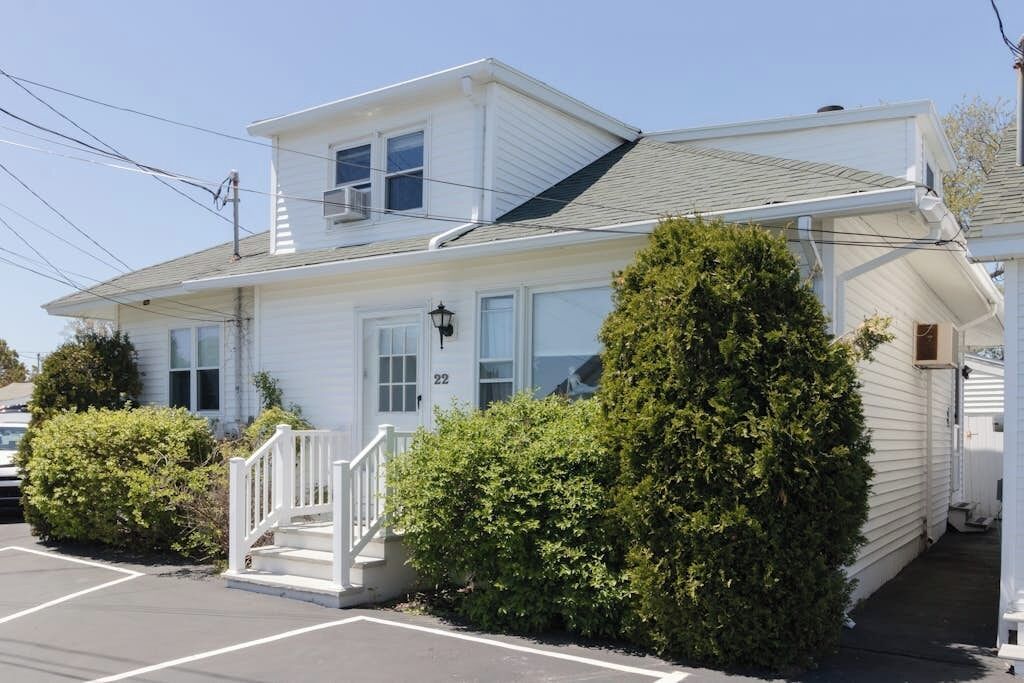 A white two-story house with a front porch, a garage, and a parking lot.