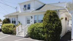 Une maison blanche à deux étages, dotée d’un porche à l’avant, d’un garage et d’un parking.