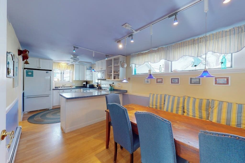 A kitchen with a central island, dining table with chairs, and a window with curtains.