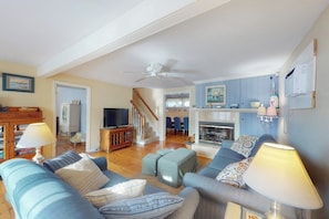 A living room with a sofa, ottoman, TV, fireplace, and a staircase leading to another room.