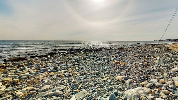 Une plage rocheuse parsemée de galets, sous un ciel dégagé.