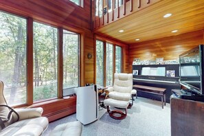 A cozy cabin interior with large windows, a piano, a television, and a comfortable seating area. - Charming Hillside Retreat with Hot Tub, Firepit, and Spacious Deck (Wells)