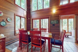 A wooden-paneled room with a dining table and chairs, large windows, and a view of the outdoors. - Charming Hillside Retreat with Hot Tub, Firepit, and Spacious Deck (Wells)