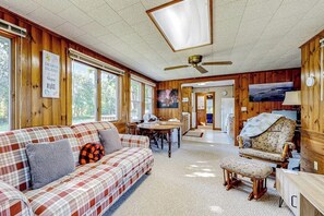 Interior acolhedor de uma cabana com um sofá xadrez, uma mesa de jantar de madeira e um ventilador de teto.