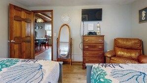 A room with two beds, a wooden dresser, a leather chair, a mirror, and a television on the wall. - Cozy Cottage with Private Deck - Walk to Short Sands Beach (York)